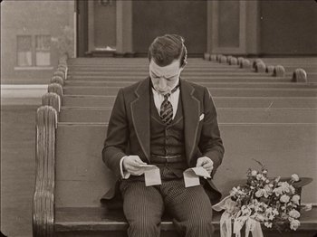 Movie still from “Seven Chances” (1925), directed by Buster Keaton – A black and white photo of a man sitting on a bench; Medium shot, High angle