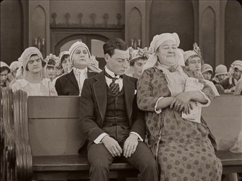Movie still from “Seven Chances” (1925), directed by Buster Keaton – An old photo of a man and a woman sitting on a bench; Medium shot, Low angle