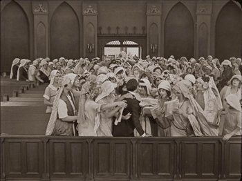 Movie still from “Seven Chances” (1925), directed by Buster Keaton – A group of people standing in front of a building; Wide shot, High angle