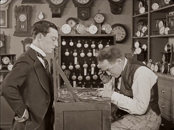 Movie still from “Seven Chances” (1925), directed by Buster Keaton – Two men in suits and ties are looking at clocks in an antique store; Medium shot, High angle