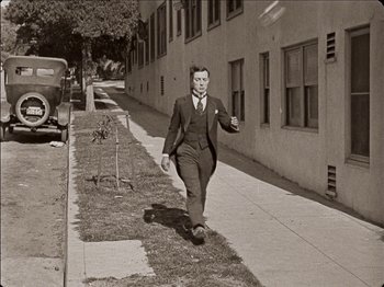 Movie still from “Seven Chances” (1925), directed by Buster Keaton – A black and white photo of a man walking down a sidewalk; Wide shot, Low angle