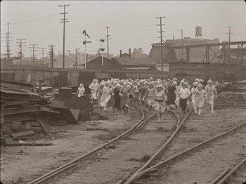 Movie still from “Seven Chances” (1925), directed by Buster Keaton – A group of people walking on train tracks near railroad tracks; Extreme Wide shot, High angle