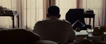 Movie still from “Seven Pounds” (2008), directed by Gabriele Muccino – A man sitting on a couch in front of a window; Medium shot, Over the shoulder angle