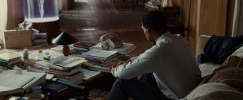 Movie still from “Seven Pounds” (2008), directed by Gabriele Muccino – A man sitting on the floor next to a pile of books; Wide shot, High angle