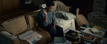 Movie still from “Seven Pounds” (2008), directed by Gabriele Muccino – A man sitting on a couch talking on a phone; Medium shot, High angle
