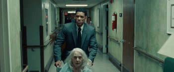 Movie still from “Seven Pounds” (2008), directed by Gabriele Muccino – A man in a suit and tie standing next to an older woman; Medium shot, Over the shoulder angle