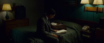 Movie still from “Seven Pounds” (2008), directed by Gabriele Muccino – A man in a suit sitting on a bed reading a book; Medium shot, High angle