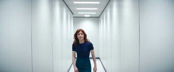 Movie still from “Severance” (2022), created by Dan Erickson – A woman in a blue shirt and blue skirt in a white hallway; Medium shot, Low angle
