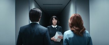 Movie still from “Severance” (2022), created by Dan Erickson – A woman holding a stack of papers standing between two men; Medium shot, Over the shoulder angle