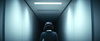 Movie still from “Severance” (2022), created by Dan Erickson – A person with a mask is walking down a hallway; Wide shot, Over the shoulder angle