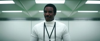 Movie still from “Severance” (2022), created by Dan Erickson – A man wearing a white sweater and a black neck cord; Close Up shot, Low angle