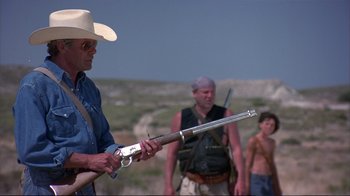 Movie still from “Sexy Beast” (2000), directed by Jonathan Glazer – A man holding a gun while standing next to two other men; Medium shot, Over the shoulder angle