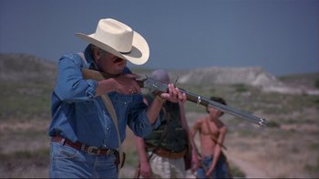 Movie still from “Sexy Beast” (2000), directed by Jonathan Glazer – A man in a cowboy hat is holding a rifle; Medium shot, Over the shoulder angle