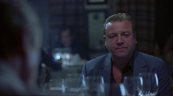 Movie still from “Sexy Beast” (2000), directed by Jonathan Glazer – A man sitting at a table with a glass of wine in front of him; Close Up shot, Over the shoulder angle