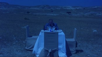 Movie still from “Sexy Beast” (2000), directed by Jonathan Glazer – A man sitting at a dinner table in the middle of a field; Wide shot, High angle