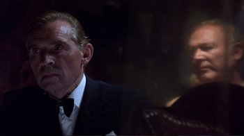 Movie still from “Sexy Beast” (2000), directed by Jonathan Glazer – An older man in a suit sitting in front of a guitar; Close Up shot, Low angle