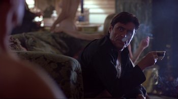 Movie still from “Sexy Beast” (2000), directed by Jonathan Glazer – A man sitting on a couch smoking a cigarette; Medium shot, Over the shoulder angle