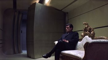 Movie still from “Sexy Beast” (2000), directed by Jonathan Glazer – A man in a suit sitting on top of a white couch; Wide shot, Low angle