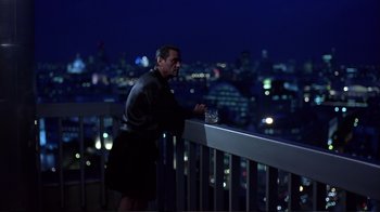 Movie still from “Sexy Beast” (2000), directed by Jonathan Glazer – A man standing on a balcony at night with a drink; Wide shot, High angle