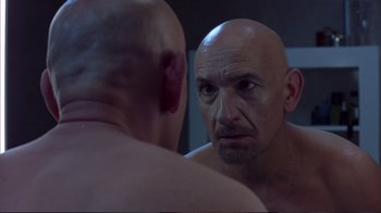 Movie still from “Sexy Beast” (2000), directed by Jonathan Glazer – A bald man looking into a mirror in front of a mirror; Close Up shot, Over the shoulder angle