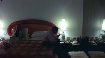 Movie still from “Sexy Beast” (2000), directed by Jonathan Glazer – A man sitting on a bed looking at his phone; Medium shot, High angle