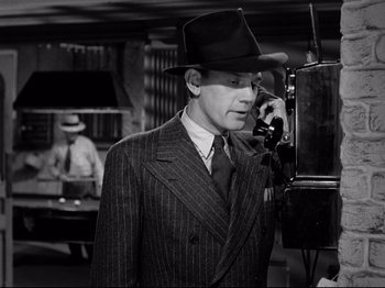 Movie still from “Shadow of a Doubt” (1943), directed by Alfred Hitchcock – A man wearing a suit and hat talking on a phone; Medium shot, Low angle