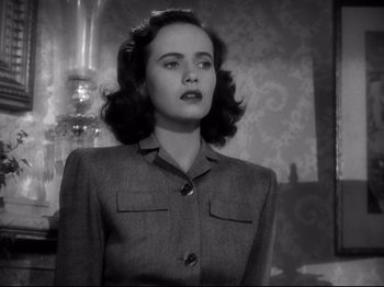 Movie still from “Shadow of a Doubt” (1943), directed by Alfred Hitchcock – A woman in a gray suit standing in front of a mirror; Close Up shot, Low angle