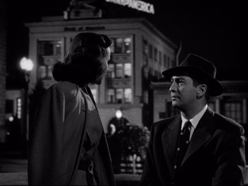 Movie still from “Shadow of a Doubt” (1943), directed by Alfred Hitchcock – A man and a woman standing next to each other in front of a building at night; Medium shot, Low angle