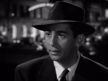 Movie still from “Shadow of a Doubt” (1943), directed by Alfred Hitchcock – A black and white photo of a man wearing a suit and a hat; Close Up shot, Over the shoulder angle