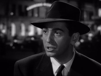 Movie still from “Shadow of a Doubt” (1943), directed by Alfred Hitchcock – A black and white photo of a man wearing a suit and a hat; Close Up shot, Over the shoulder angle