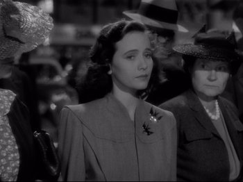 Movie still from “Shadow of a Doubt” (1943), directed by Alfred Hitchcock – A woman wearing a suit and hat in a crowd of people; Close Up shot, Over the shoulder angle
