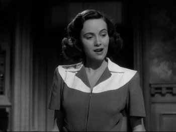 Movie still from “Shadow of a Doubt” (1943), directed by Alfred Hitchcock – A woman in a brown and white dress standing in front of a window; Medium shot, Low angle