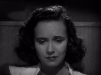 Movie still from “Shadow of a Doubt” (1943), directed by Alfred Hitchcock – A woman sitting in front of a wooden wall with her eyes closed; Close Up shot, High angle