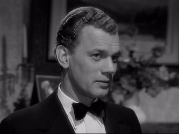 Movie still from “Shadow of a Doubt” (1943), directed by Alfred Hitchcock – A man wearing a suit and bow tie in front of a wall; Close Up shot, Low angle