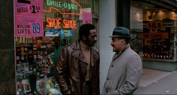 Movie still from “Shaft” (1971), directed by Gordon Parks – Two men standing next to each other in front of a shoe store; Medium shot, Over the shoulder angle
