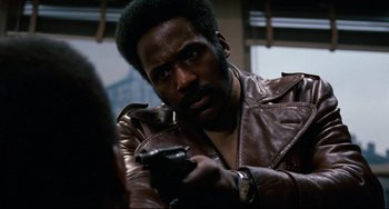 Movie still from “Shaft” (1971), directed by Gordon Parks – A man holding a gun while wearing a leather jacket; Close Up shot, Low angle