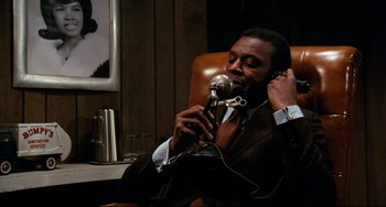 Movie still from “Shaft” (1971), directed by Gordon Parks – A man sitting in a leather chair holding a microphone; Close Up shot, Low angle