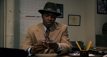 Movie still from “Shaft” (1971), directed by Gordon Parks – A man wearing a suit and a hat is playing cards; Medium shot, Over the shoulder angle