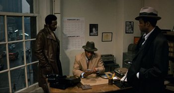 Movie still from “Shaft” (1971), directed by Gordon Parks – A man sitting at a desk in front of another man; Medium shot, Over the shoulder angle