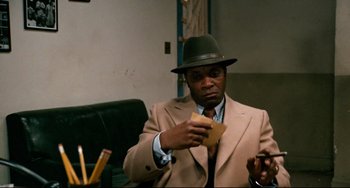 Movie still from “Shaft” (1971), directed by Gordon Parks – A man wearing a hat and a suit holding a piece of paper; Medium shot, Over the shoulder angle