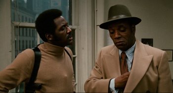 Movie still from “Shaft” (1971), directed by Gordon Parks – A man in a suit and a man in a hat; Medium shot, Over the shoulder angle