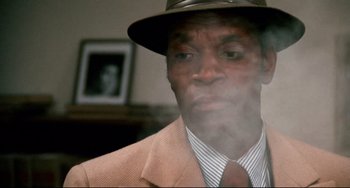 Movie still from “Shaft” (1971), directed by Gordon Parks – A man wearing a suit and a hat is smoking; Close Up shot, Low angle