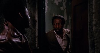 Movie still from “Shaft” (1971), directed by Gordon Parks – A man standing in a room next to a door; Medium shot, Over the shoulder angle