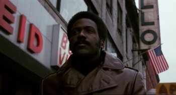 Movie still from “Shaft” (1971), directed by Gordon Parks – A man in a brown jacket standing in front of a building; Close Up shot, Low angle