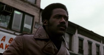 Movie still from “Shaft” (1971), directed by Gordon Parks – A man in a brown jacket standing in front of a building; Close Up shot, Low angle