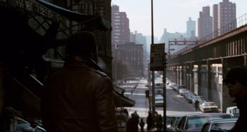 Movie still from “Shaft” (1971), directed by Gordon Parks – A man in a brown jacket is standing on a street; Wide shot, Over the shoulder angle