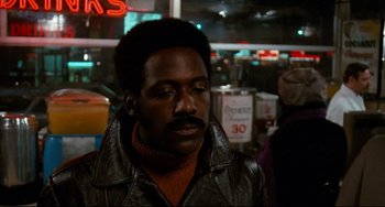 Movie still from “Shaft” (1971), directed by Gordon Parks – A man in a leather jacket standing next to a neon sign; Close Up shot, Over the shoulder angle