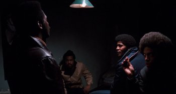 Movie still from “Shaft” (1971), directed by Gordon Parks – A group of men standing around in a room; Medium shot, Over the shoulder angle