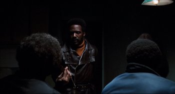 Movie still from “Shaft” (1971), directed by Gordon Parks – A group of people that are standing in a room; Medium shot, Over the shoulder angle