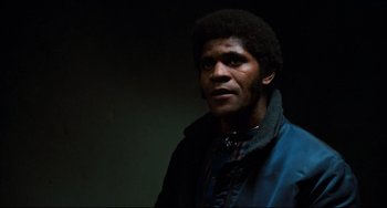 Movie still from “Shaft” (1971), directed by Gordon Parks – A man in a blue jacket is standing in a dark room; Close Up shot, Low angle